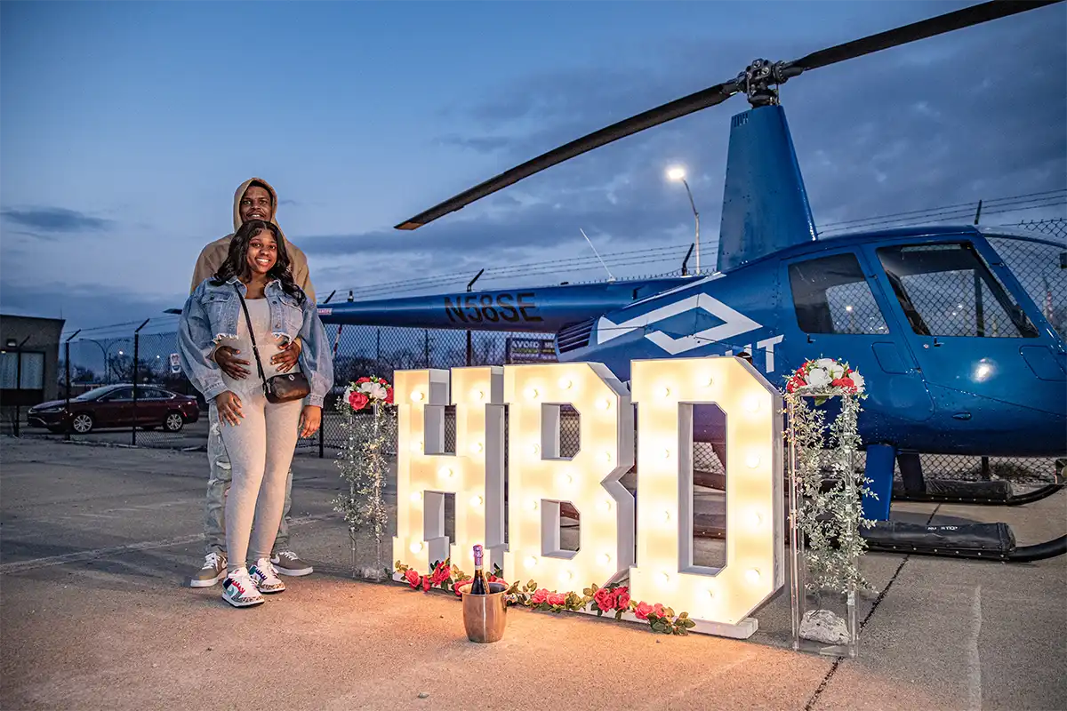 a couple standing next a 4ft tall marquee lit up sign that says HBD after a helicopter tour with MyFlight Tours