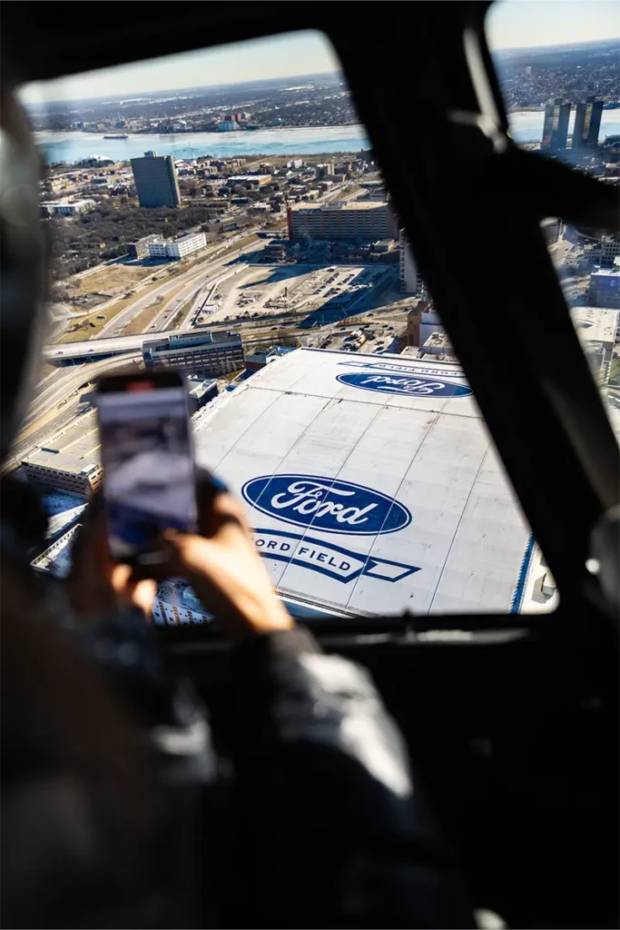 a person with an iphone taking a picture of ford field in downtown detroit from a helicopter tour